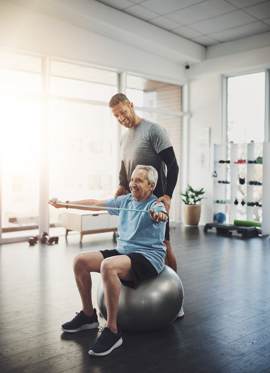 Stretching, senior man and physiotherapist with band for resistance training, support or muscle workout. Fitness, physiotherapy and happy elderly person with ball for mobility exercise in retirement